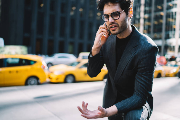 Annoyed professional manager annoyed during mobile phone conversation standing on avenue, angry businessman in suit worried about problem discusing solution through telephone talk gesturing in cit - Fotoğraf, Görsel