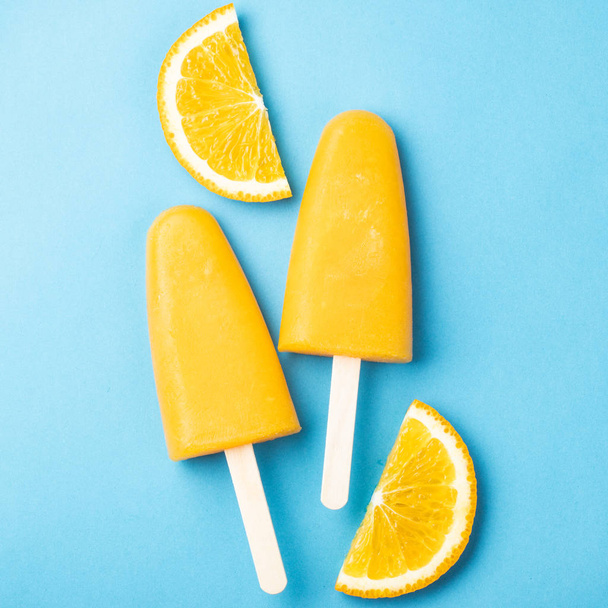 Orange popsicles with juice on a blue background. Ice pops, flat lay, top view. - Фото, зображення