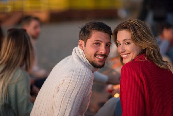 Young Couple enjoying with friends Around Campfire on The Beach At sunset drinking beer - Photo, Image