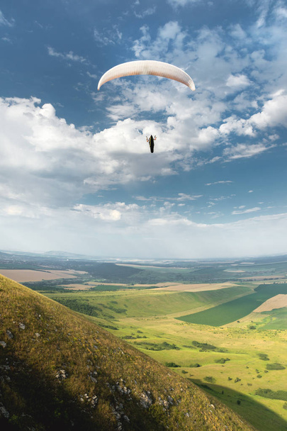 White orange paraglide with a paraglider in a cocoon against the background of fields of the sky and clouds. Paragliding Sports - Photo, Image