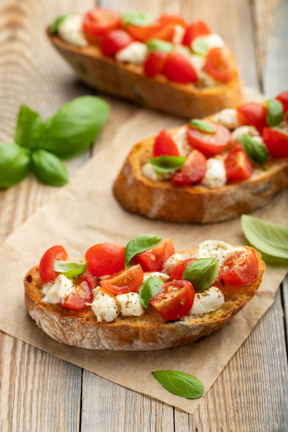 Bruschetta with tomatoes, mozzarella cheese and basil on a old rustic table. Traditional italian appetizer or snack, antipasto. - Photo, Image