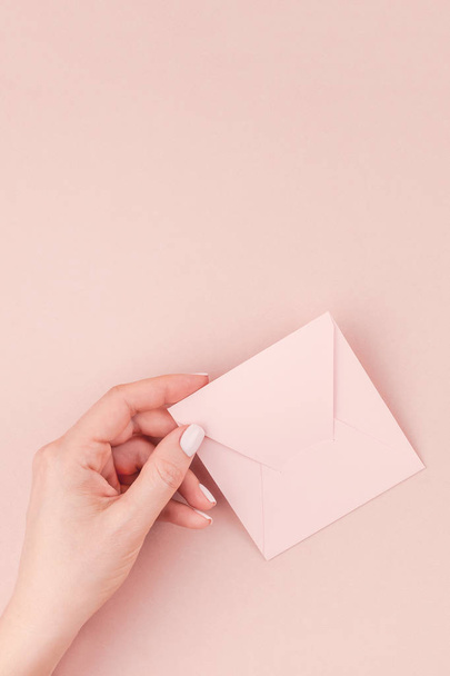 Creative image of woman hand holding small love letter with copy space on millennial pink background in minimalism style. Concept template for feminine blog, social media - Фото, зображення