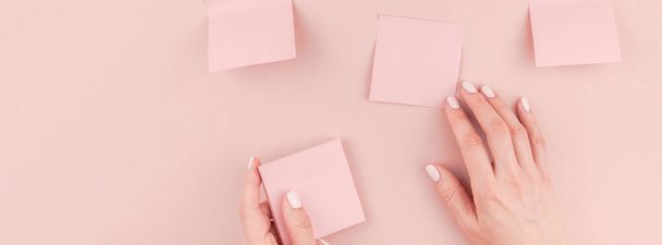 Long wide banner of workspace desk with millennial pink sticker paper post it mock up in woman hands holding and gluing them on wall with copy space background minimal style. Template for text - Zdjęcie, obraz