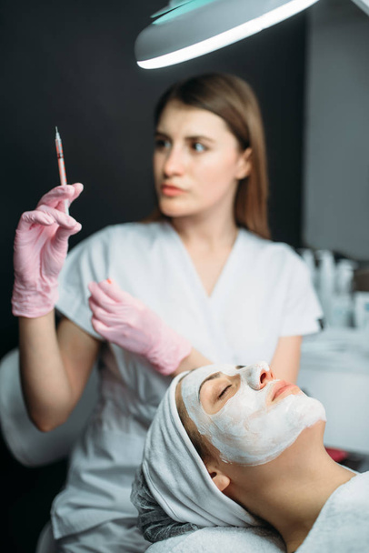 美容師に対する女性患者、ボトックス注射、しわ、美容クリニックの手で注射器。顔スキンケア、スパのサロン、医療で若返りの手順 - 写真・画像