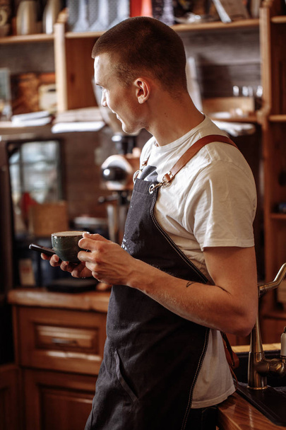 close up back view photo of cheerful waiter with a cup of coffee and a mobile phone - Fotó, kép