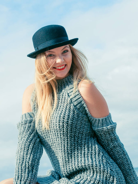Beautiful young blonde woman wearing fedora hat and sweater jumper posing on sky background. - Фото, изображение