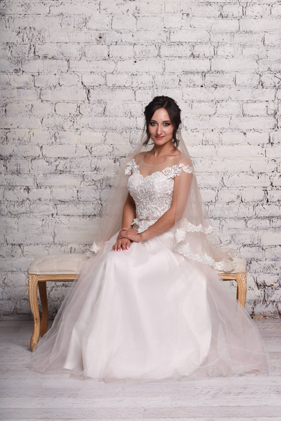 Young brunette bride in white elegance wedding dress posing in front of brick wall - Photo, image