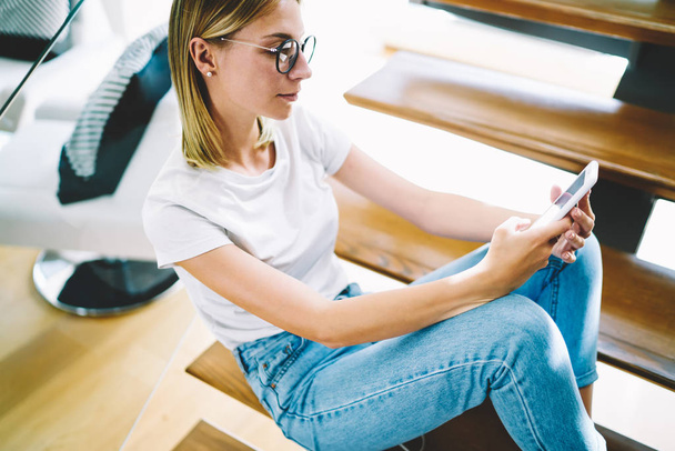 Cropped image of charming female person dressed in casual clothes checking notification on smartphone connected to home internet. Good looking woman enjoying recreation indoors using modern technology - Фото, изображение