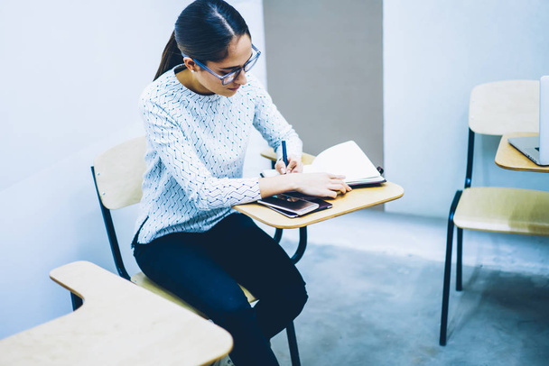 Clever female student sitting at desk in classroom concentrated on writing final test quiz in college, smart young woman studying on courses making notes for doing university coursework project - Foto, Bild