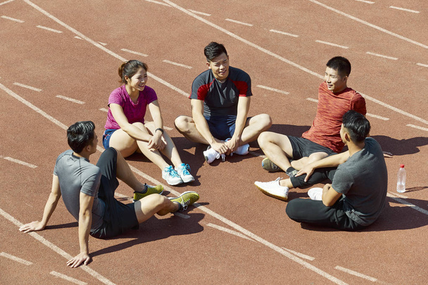 Skupina mladých asijských sportovců sedí, mluvící chatování na dráze. - Fotografie, Obrázek