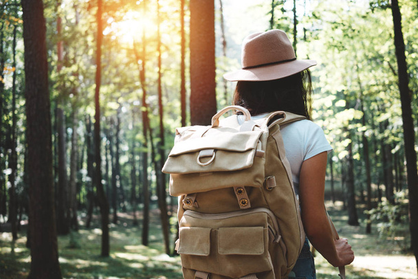 Back view on handsome traveler hipster girl with backpack and hat walking in forest among trees - Фото, зображення