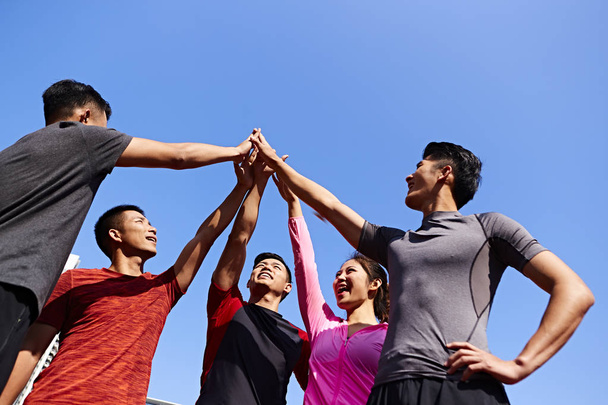 команда взрослых азиатских спортсменов и спортсменок объединяются, чтобы показать единство и командный дух
. - Фото, изображение