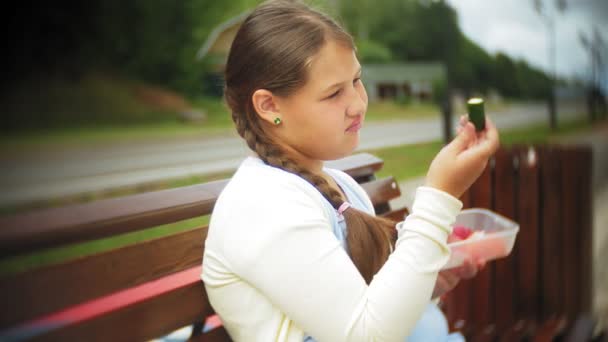 Close up of adorable little fat girl eating vegetables with her hands sitting on a bench in the park, concept of healthy eating - Materiał filmowy, wideo