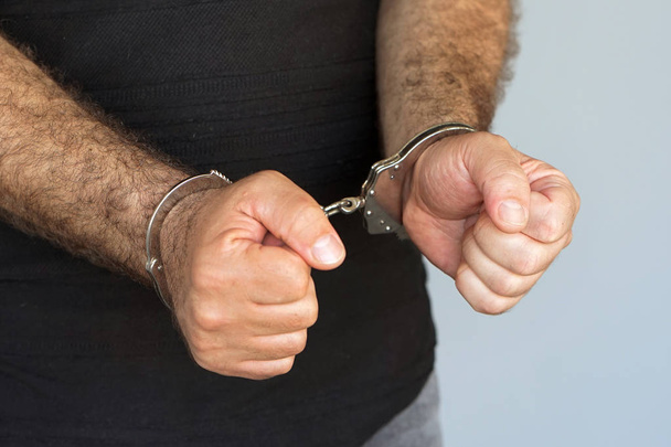 Close-up. Homem detido algemado mãos isoladas em fundo cinzento. Prisioneiro ou preso terrorista, fechar as mãos algemado
. - Foto, Imagem