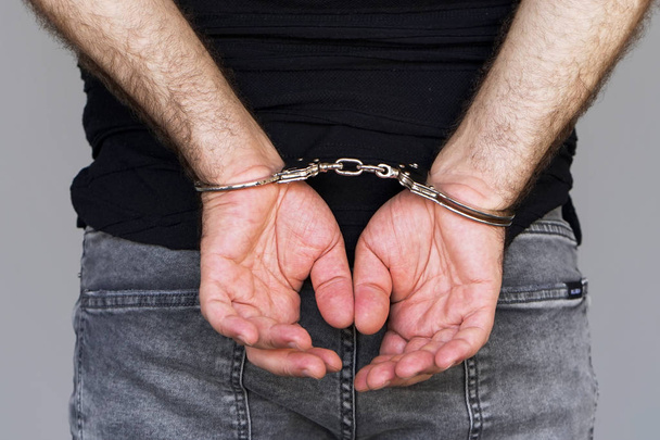 Close-up. Gearresteerde man geboeid handen geïsoleerd op een grijze achtergrond. Gevangene of gearresteerd terrorist, close-up van handen in handboeien. - Foto, afbeelding