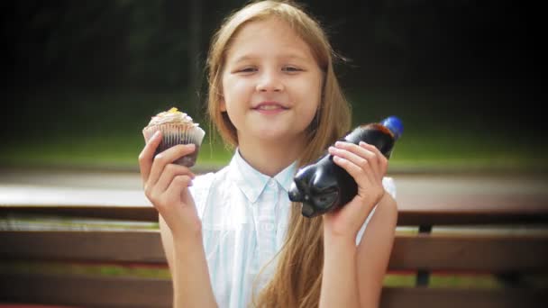 Aranyos kislány eszik süteményt, kezével ül egy padon a parkban közelről - Felvétel, videó