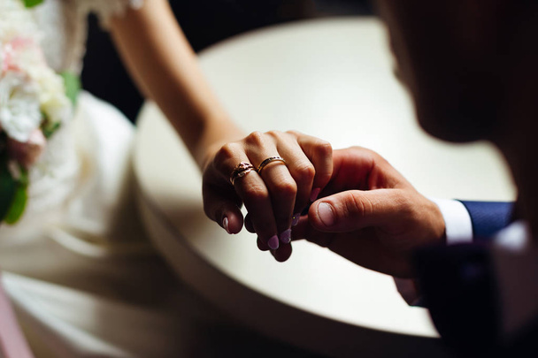 Nahaufnahme der Hand der Braut mit schönen Ringen, die der Bräutigam hält und sie sitzen am Tisch - Foto, Bild