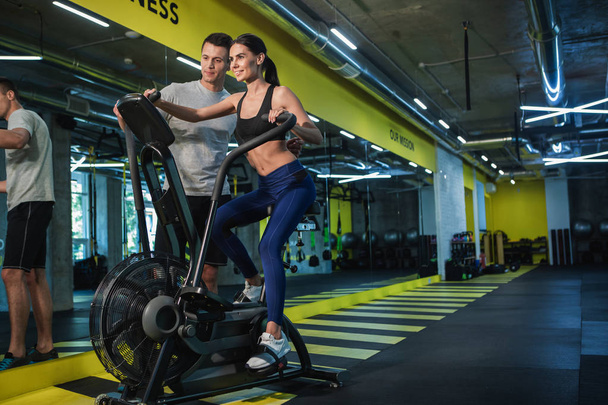 Instructor is helping woman training with machine indoors - Foto, imagen
