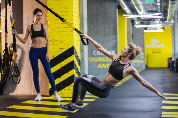 Two women are exercising with trx system in turn - Фото, зображення