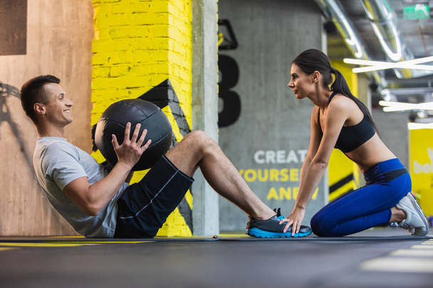 Positive man is doing crunches with woman assistance - Photo, Image