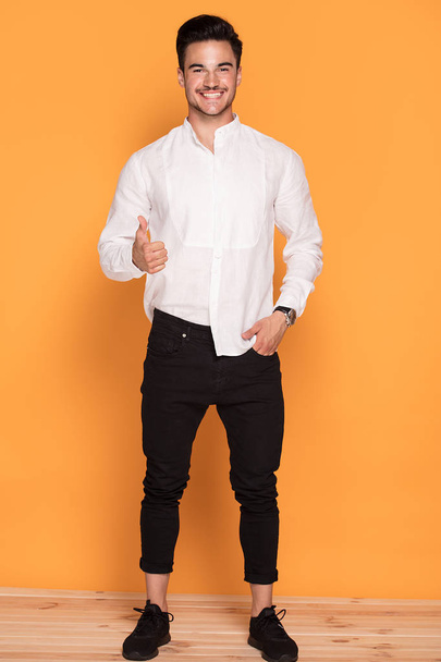 Photo of smiling handsome young man in elegant fashionable clothes on yellow studio background. - Photo, Image
