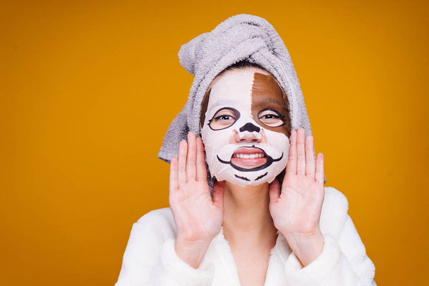 cheerful girl with a towel on her head wants to be beautiful, on her face a moisturizing mask with a dog's face - Foto, Imagen