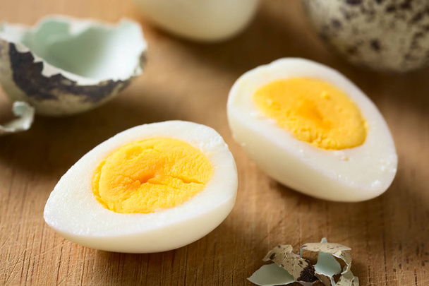 Жесткий перепелиное яйцо половинки с яичной скорлупой на деревянной доске, фотографируется с естественным светом (селективный фокус, фокус в середине левого яйца половина
) - Фото, изображение
