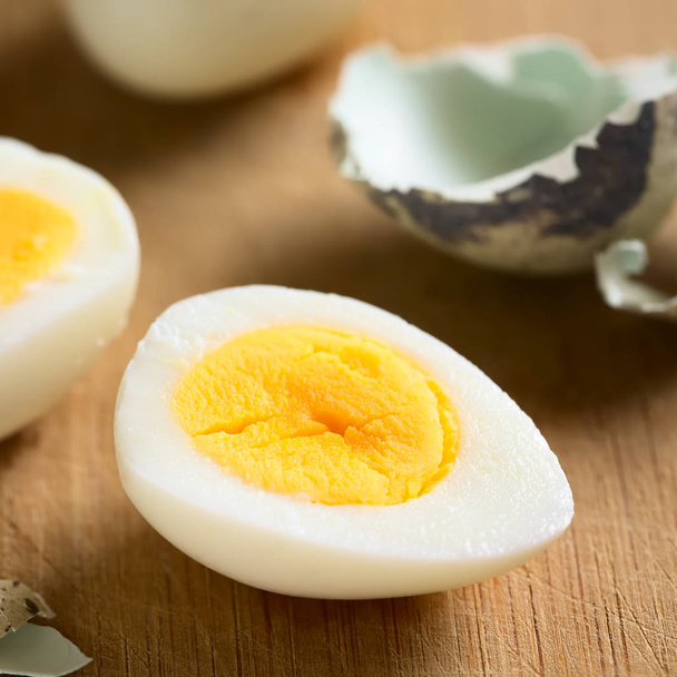 Жесткий перепелиное яйцо наполовину с яичной скорлупой на деревянной доске, фотографируется с естественным светом (селективный фокус, фокус в середине яйца половина
) - Фото, изображение