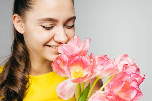 charming smiling girl in a yellow dress smelling beautiful pink flowers - Fotó, kép