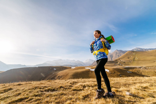 active young girl in a blue jacket travels through the Caucasus mountains with a backpack - Фото, изображение