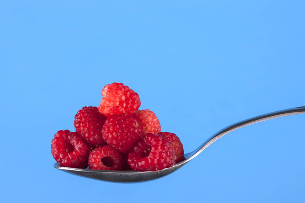 Ripe red raspberries piled on a spoon set against a blue background. - Photo, Image