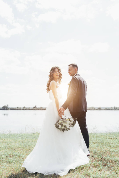 couple in wedding attire with a bouquet of flowers and greenery is in the hands against the backdrop of the field at sunset, the bride and groom - Fotó, kép
