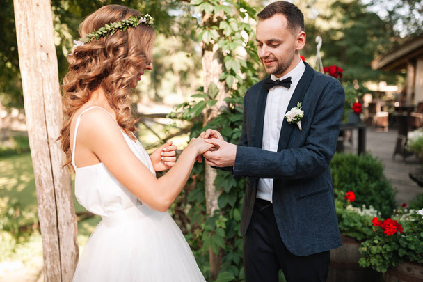 Beauty bride and handsome groom are wearing rings each other. Wedding couple on the marriage ceremony. Beautiful model girl in white dress. Man in suit. Female and male portrait. Cute lady and guy - Fotó, kép