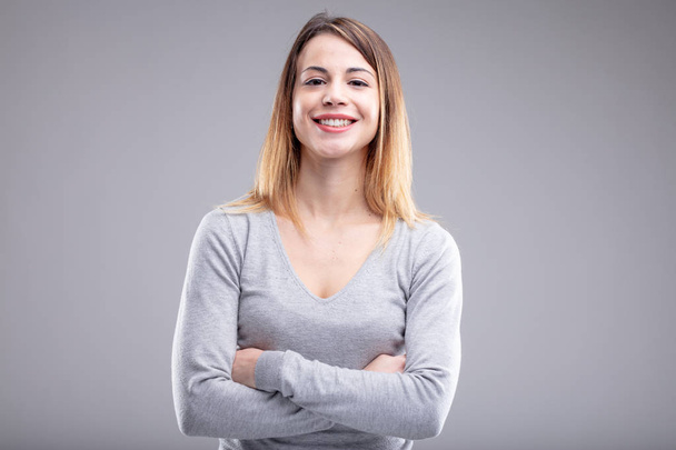 Una giovane donna felice con le braccia incrociate e indossa una camicia grigia su sfondo grigio chiaro. Include spazio di copia
. - Foto, immagini