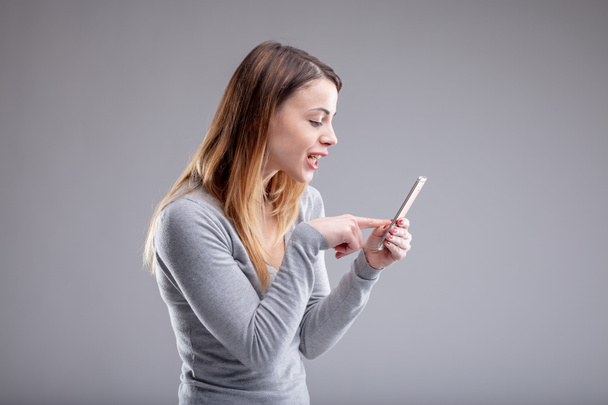 Una mujer adulta con cabello castaño largo mirando de cerca el teléfono inteligente blanco mientras lo toca. Incluye espacio de copia
. - Foto, Imagen
