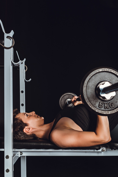 side view of young female athlete doing exercise with barbell, black background - Photo, Image