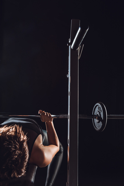 partial view of female athlete doing exercise with barbell, black background - Foto, imagen