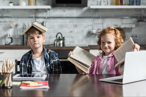 чарівні маленькі діти з великою кількістю книг, які дивляться на камеру на кухні
 - Фото, зображення