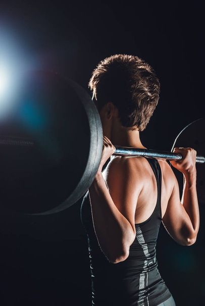 side view of sportswoman exercising with barbell, black background - Фото, зображення