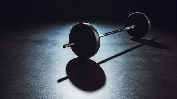 vue rapprochée de l'haltère sur le sol avec ombre à la salle de gym, fond noir
  - Photo, image