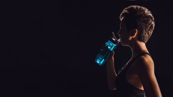 Zijaanzicht van Sportvrouw drinkwater uit de fles, zwarte achtergrond  - Foto, afbeelding