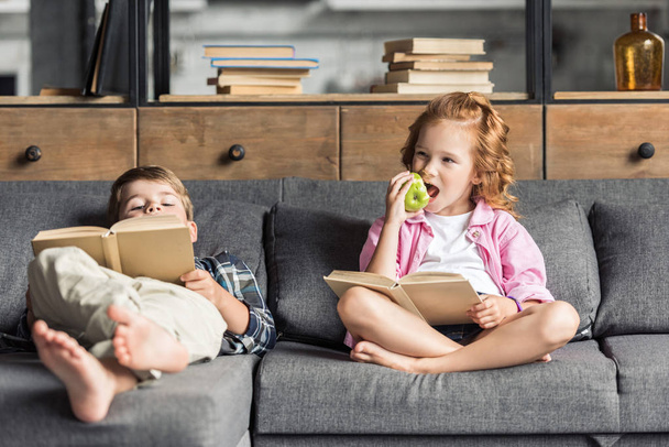 cute little brother and sister reading books on couch at home - Foto, Bild