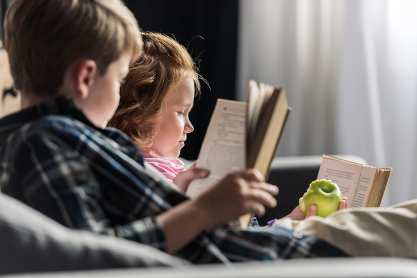 little brother and sister reading books on couch at home - Foto, Imagen
