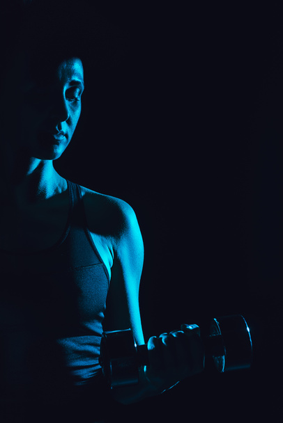 тонизированная фотография спортсменки, занимающейся спортом с гантелями, черным фоном
  - Фото, изображение