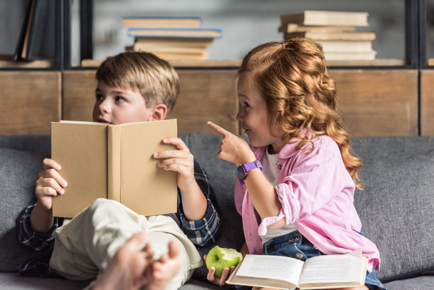 cute little schoolboy reading book on couch while his sister pointing somewhere - Photo, Image