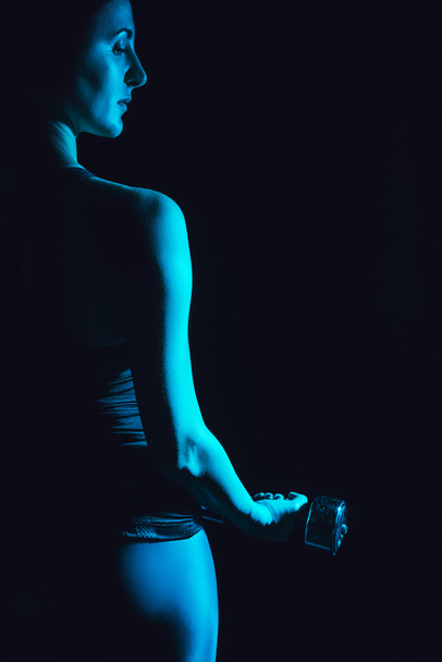 toned picture of young sportswoman exercising with dumbbell, black background  - Foto, immagini