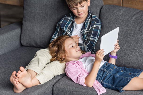 adorable little brother and sister using tablet together while relaxing on couch - Photo, image