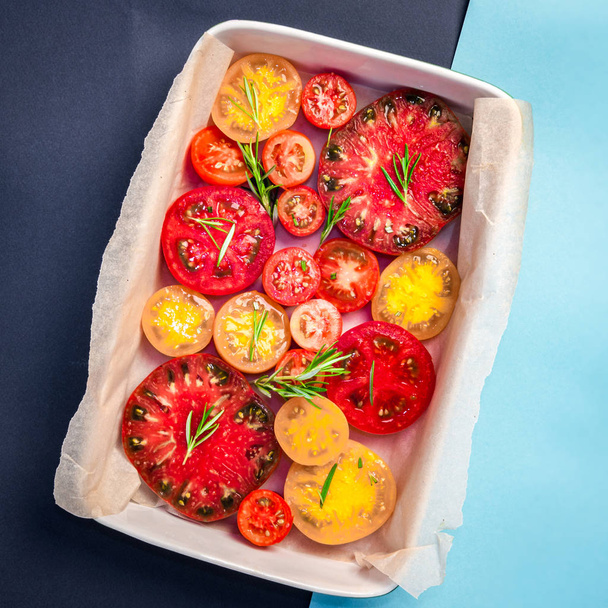 Pie with tomatoes, olive oil, Parmesan cheese and rosemary on parchment paper into ceramic dish. Light blue and navy blue paper background, copy space, top view - Foto, Imagem