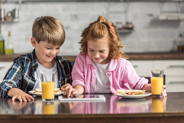 happy little brother and sister using tablet during breakfast at kitchen - Fotografie, Obrázek