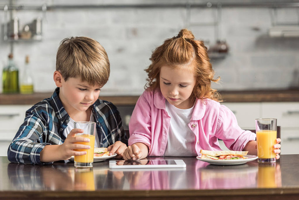 adorable little brother and sister using tablet during breakfast - Фото, изображение